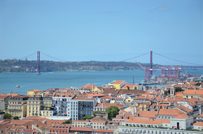 5 - A high-angle view over the terracotta rooftops of Lisbon, Portugal, looking across the Tagus River toward the iconic red suspension bridge